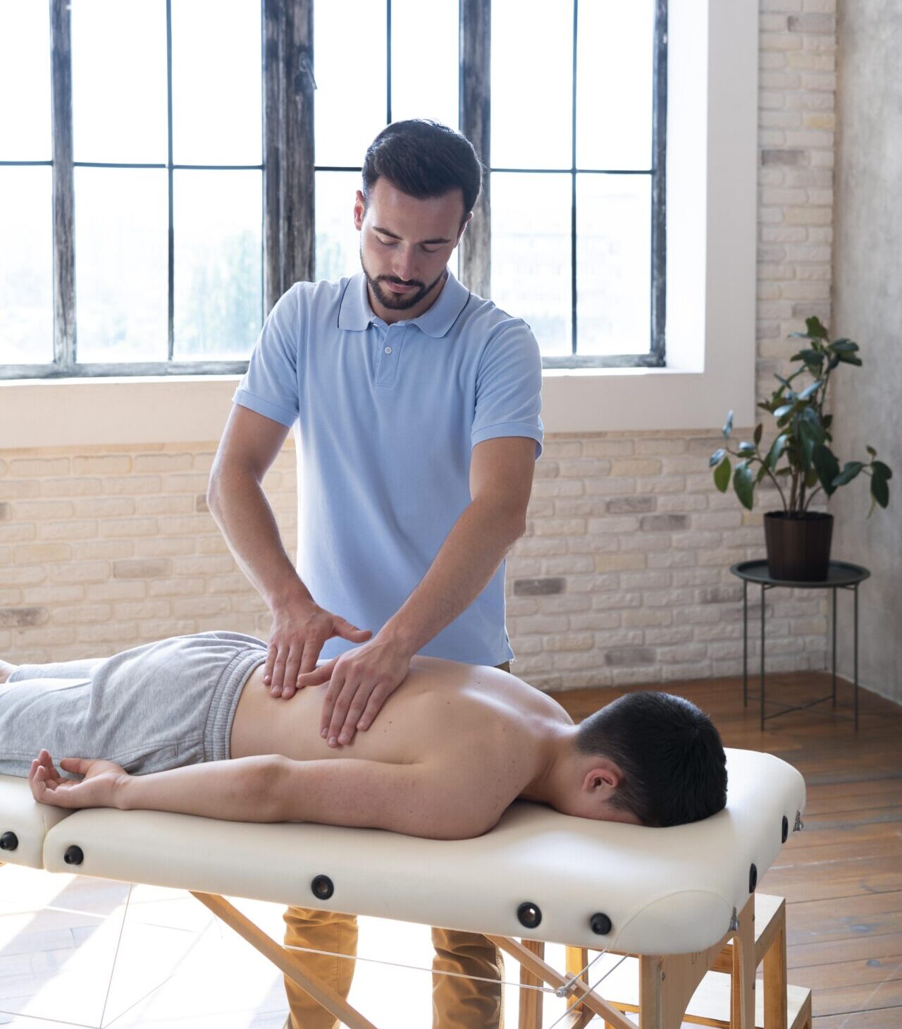 Fizjoterapeuta masażysta wykonuje masaż klasyczny pleców pacjentowi leżącego na leżance